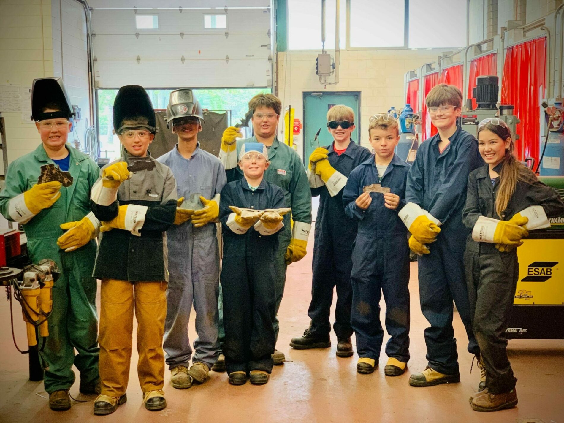 Kids in welding equipment holding welded parts
